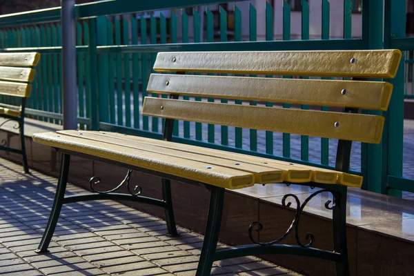 Banco amarillo en el fondo de la cerca de metal verde — Foto de Stock