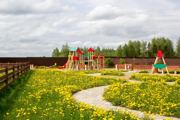 Parque infantil entre dentes-de-leão florescentes — Fotografia de Stock