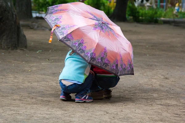 Niño y niña escondidos bajo un paraguas en las horcas — Foto de Stock