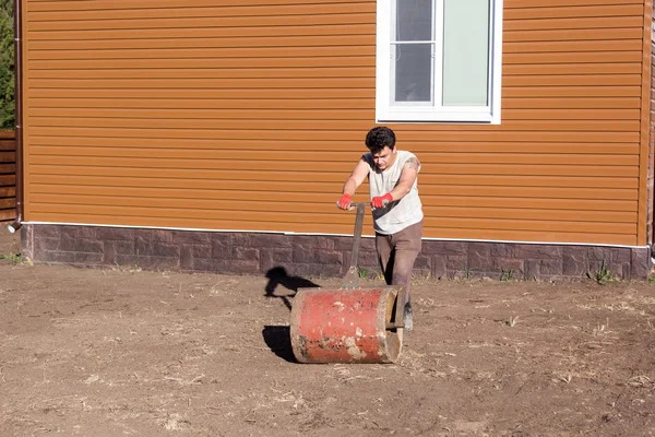 Mężczyzna zagęszcza gleby z ręki metalowy walec — Zdjęcie stockowe