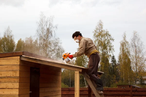 Человек красит деревянное укрытие спреем — стоковое фото