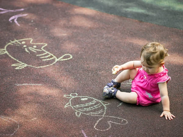 小女孩将一支粉笔绘制在操场上 — 图库照片