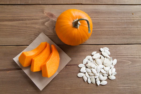 Pumpkin slices on parchment paper, seeds and the whole pumpkin — Stock Photo, Image