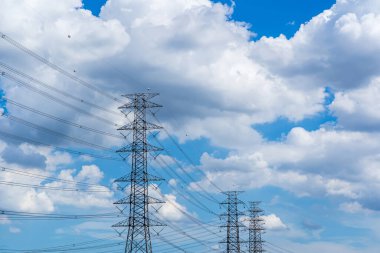 Mavi bulutlu gökyüzüne karşı yüksek voltajlı elektrik direği.