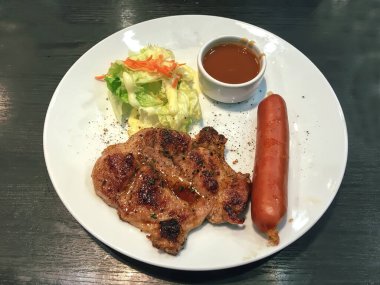 Sosisli ızgara domuz eti, taze salata ve soslu beyaz tabak..