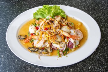 Işıl ışıl Tayland baharatlı deniz ürünleri salatasının üst görüntüsü. Karides, kalamar, midye ve otlar siyah bir masanın üzerinde beyaz bir tabakta servis ediliyor..