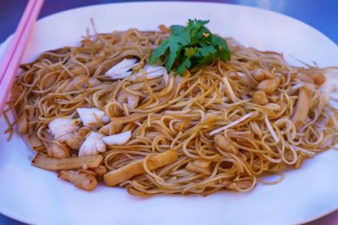 Yanında deniz ürünleri, fasulye filizi ve kişniş ile süslenmiş baharatlı kızarmış şehriye tabağı..