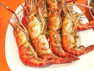 Beyaz tabakta servis edilen turuncu başlı dev nehir karidesleri..
