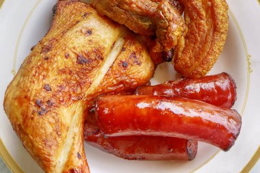 Izgara tavuk, tatlı sosis ve beyaz tabakta gevrek domuz göbeği..