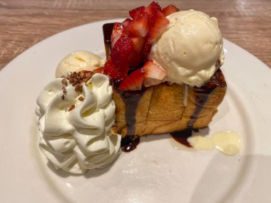 Üzerine taze çilek, çikolata sosu, çırpılmış krema ve vanilyalı dondurma konmuş hoşgörülü ballı tost zengin ve tatlı bir tatlı yaratıyor..