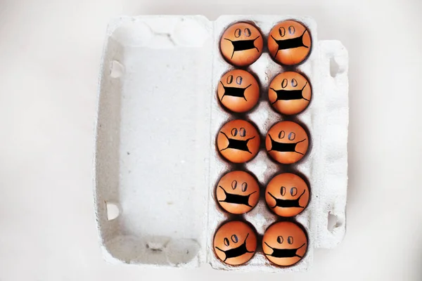 chicken eggs with drawn medical mask on egg carton on a white background. Easter eggs holidays decoration.