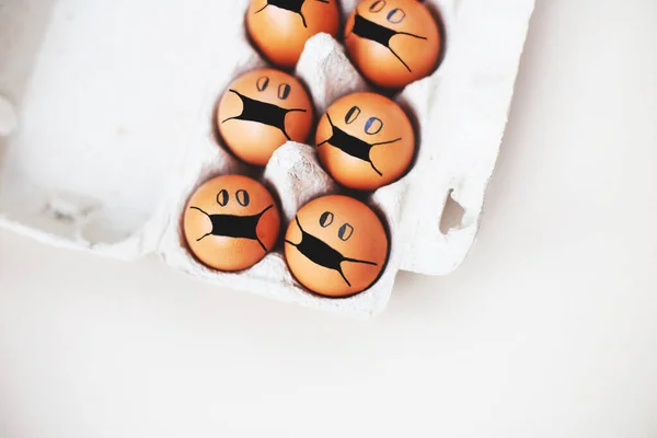 chicken eggs with drawn medical mask on egg carton on a white background. Easter eggs holidays decoration.