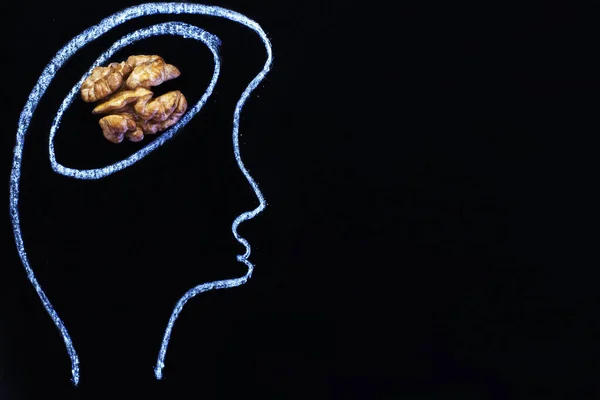 silhouette of person drawn head with nuts and abstraction brain in the form of walnut on a black background. Concept of healthy food for a human to think.