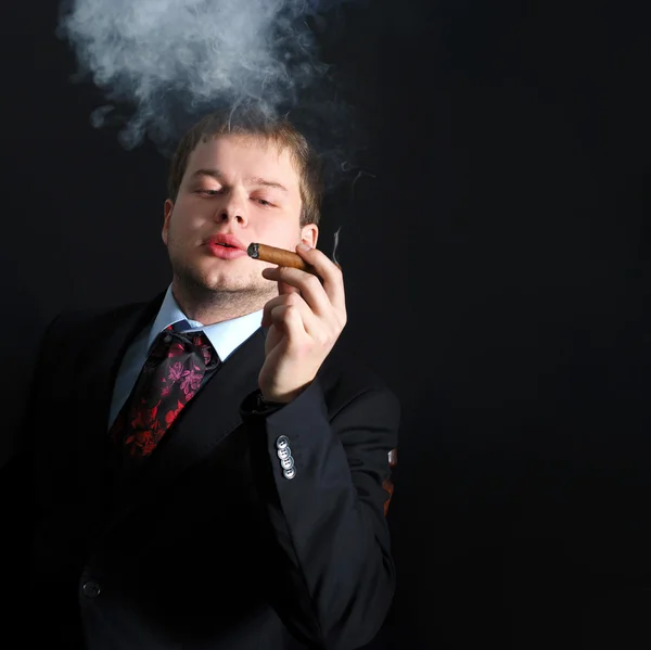Ο άνθρωπος καπνίσει ένα πούρο με τα μέρη του καπνού. Σκούρο φόντο — Φωτογραφία Αρχείου