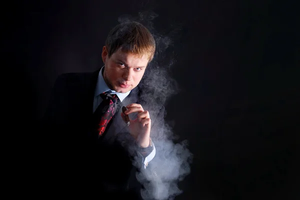 L'homme en costume fume un cigare, beaucoup de fumée. Un fond sombre — Photo