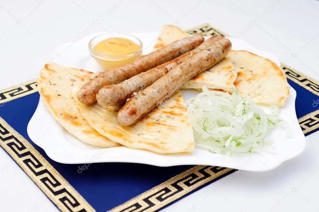 Grilled sausages, pita bread, mustard and greens on white plate