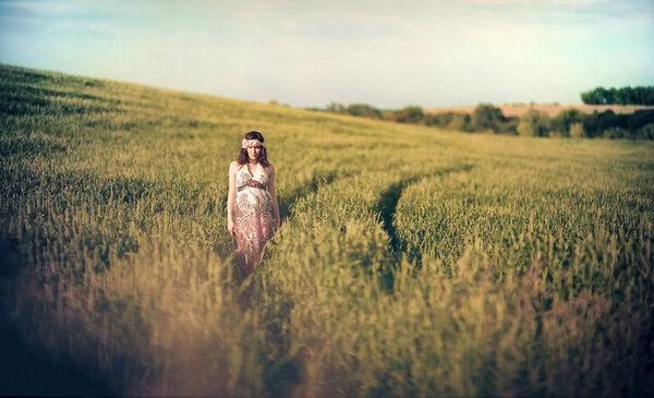 Romantic pregnant woman outside in the field and greenery like fairytale