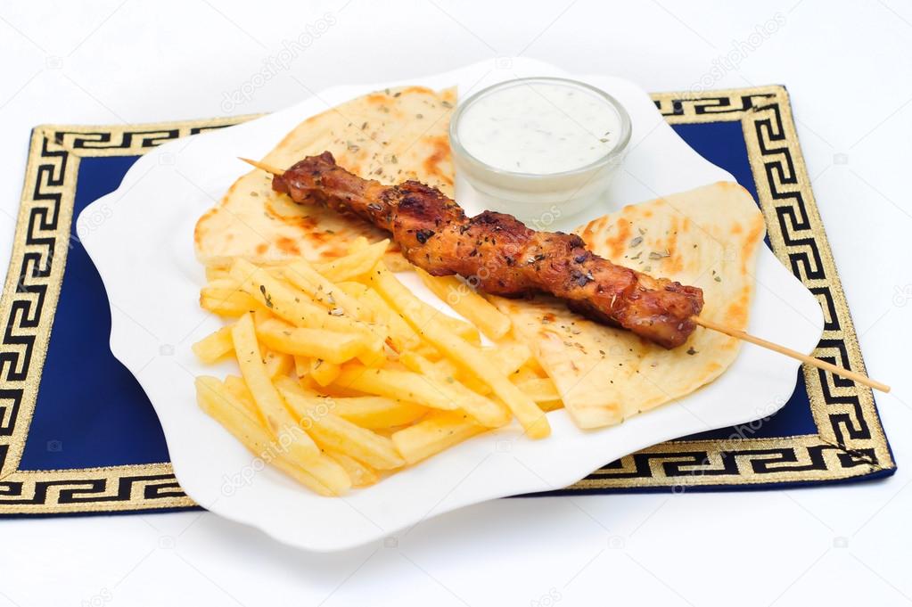 Souvlaki or kebab, grilled meat on pita bread with sauce and french fries, white plate.