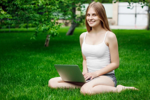 beautiful girl working at a laptop sitting on green grass