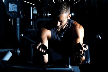 Yakışıklı ve kaslı bir adam, spor salonunda kameraya poz veriyor. 