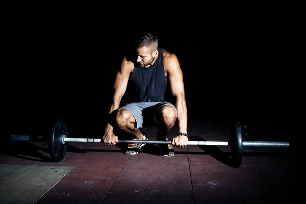 Hombre musculoso de pie de rodillas con barra en un club de gimnasio . — Foto de Stock