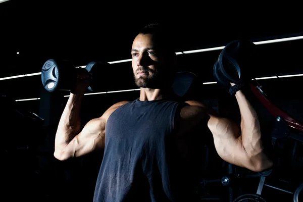 Musculoso hombre entrenando sus hombros con mancuernas — Foto de Stock
