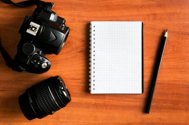 Ahşap bir masanın üzerinde boş bir not defteri olan fotoğraf makinesi ve lens. Fotoğrafçının not defteri. Fotoğraf dersleri konsepti.