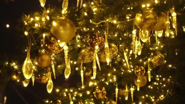 In der Nähe leuchtet ein Weihnachtsbaum, der nachts glitzert. Neujahrstanne mit Dekoration und Beleuchtung. Weihnachtsbaumschmuck Hintergrund. Viele große goldene Kugeln an Tannenbaum Neujahr und Weihnachten — Stockvideo