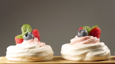 Taze böğürtlen ve nane yapraklarıyla süslenmiş üç mini Pavlova kekinin kamyonet çekimini kapat. Gri arkaplanda izole