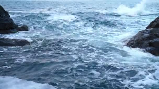 Gyengéd kék tenger hullámok rohanó és fröccsenő ellen sötét szürke sziklák alkotó fehér hab