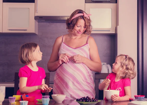 Pregnant mom with little daughters preparing cupcakes.