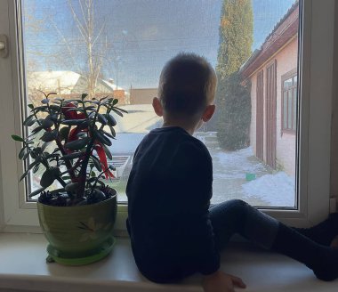 Çocuk pencereden dışarı bakar ve iş yerindeki ebeveynleri bekler. Seçici odak.