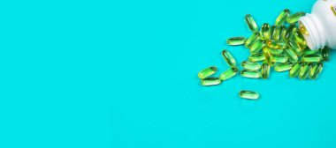 Omega 3 balık yağı kapsülleri mavi arka planda şişeden dökülüyor..