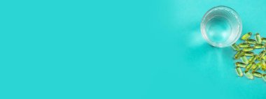 Omega 3 balık yağı kapsülleri mavi arka planda şişeden dökülüyor..