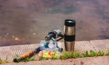 Olta kamışı, dönen makara ve nehir rıhtımında bir fincan sıcak kahve. Şehir dışında tatil kavramı. Doğa. Seçici odak