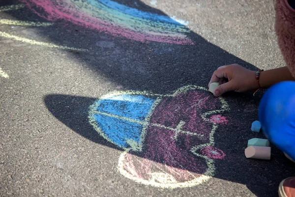 girl draws a rainbow, sun, car with chalk on the asphalt. Selective focus
