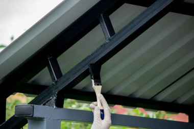 Kara metal fırçayla resim yapan bir kız. Çatıyı boyuyor. Seçici odak