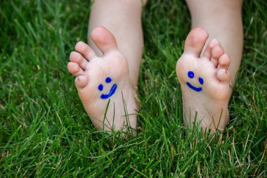 Çocuk yeşil çimlerin üzerinde yatıyordu. Bacaklarında ve kollarında boyalarla gülümse. Çocuk bahar parkında eğleniyor. Seçici odaklanma. Doğa