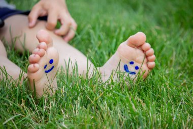 Çocuk yeşil çimlerin üzerinde yatıyordu. Bacaklarında ve kollarında boyalarla gülümse. Çocuk bahar parkında eğleniyor. Seçici odaklanma. Doğa