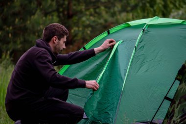 Bir adam turist çadırının yanında oturuyor. Doğa, dinlenme, kamp. Seçici odak