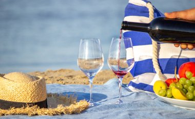 Bardaklara kırmızı şarap doldurmak, denize bakmak, deniz kenarında piknik yapmak. Seçici odak