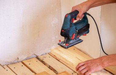 Bir adam elektrikli testereyle tahtayı keser. Evdeki zeminin tamiri. Seçici odak.