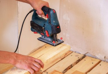 Bir adam elektrikli testereyle tahtayı keser. Evdeki zeminin tamiri. Seçici odak.