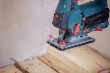 Bir adam elektrikli testereyle tahtayı keser. Evdeki zeminin tamiri. Seçici odak.