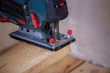 Bir adam elektrikli testereyle tahtayı keser. Evdeki zeminin tamiri. Seçici odak.