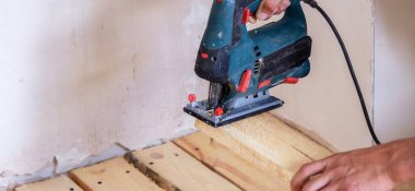 Bir adam elektrikli testereyle tahtayı keser. Evdeki zeminin tamiri. Seçici odak.