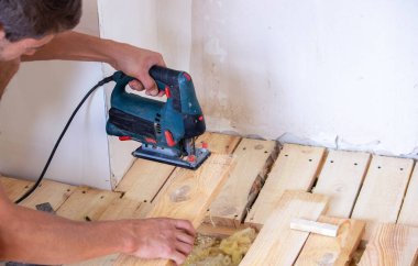 Bir adam elektrikli testereyle tahtayı keser. Evdeki zeminin tamiri. Seçici odak.