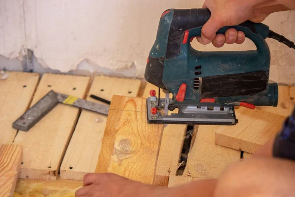 En man klipper en bräda med en elektrisk såg. Reparation av golvet i huset. Selektiv inriktning. — Stockfoto