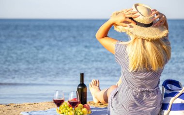 Kumsalda bir bardak şarapla gülümseyen güzel bir kadın. Meyve kırmızısı şarap. Seçici odak.