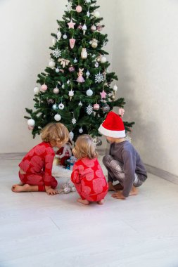 Three children in pajamas decorating a Christmas tree. Christmas Tradition.